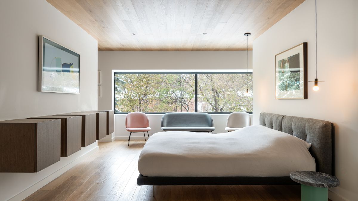 An interior shot of a spacious bedroom featuring a wide glass window, allowing for natural light and an outside view.