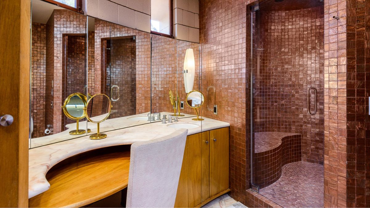 Small bathroom with tile walls, a shower area, a white clean sink with a wooden cabinet beneath it, and a large mirror.