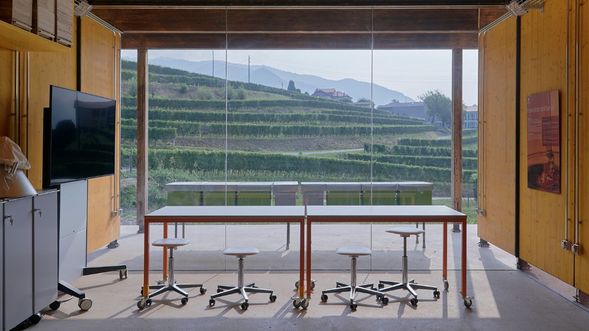 A spacious room with a scenic view in front of full height window. A U-shaped table and chairs without backrest are shown in the room along with a flat screen TV on the wall.