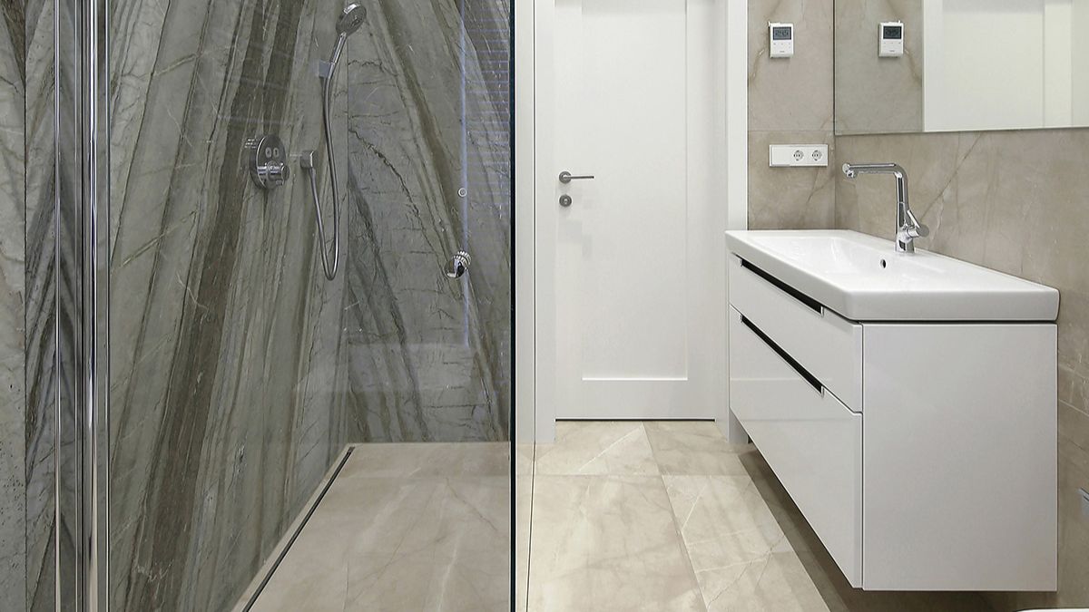 The inside perspective of the bathroom overviews the shower, sink, mirror, and white door. The marble gives a playful effect in the bathroom.