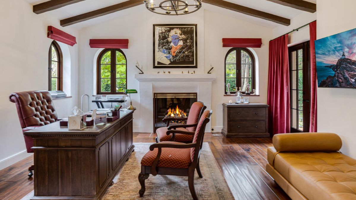 This fireplace-equipped home office space, which is located on the first floor, features a wooden floor and wood beamed ceilings.