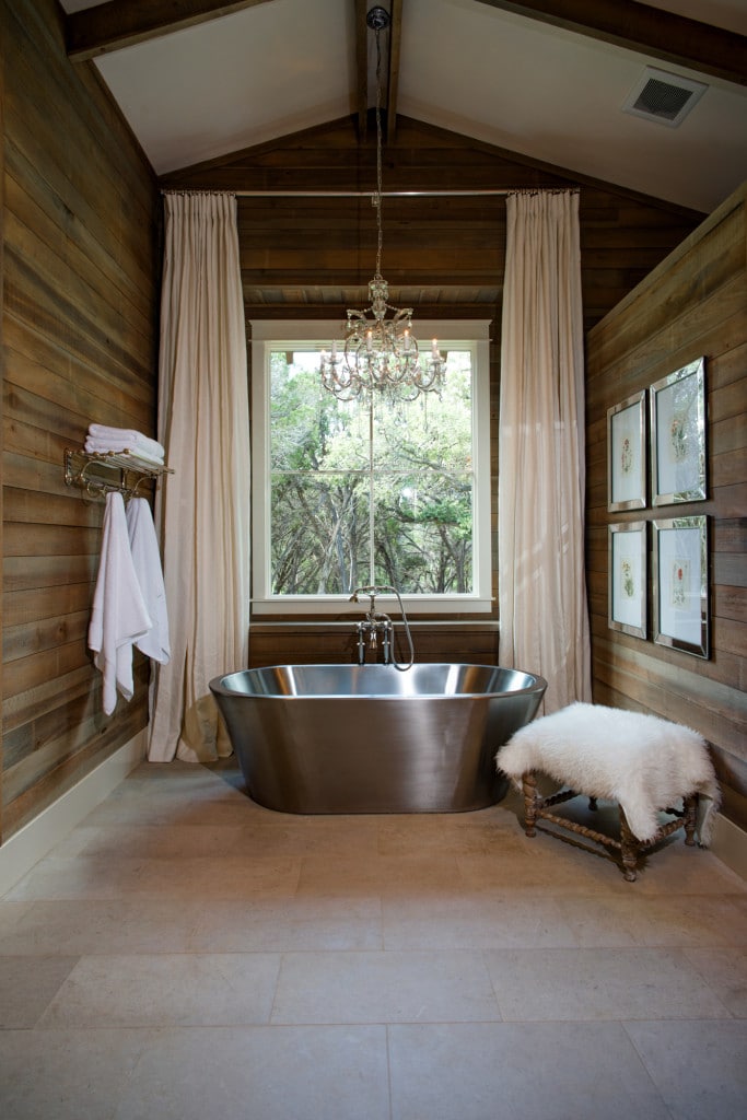 The primary bathroom is brightened by a large window and a classy crystal chandelier hanging over the freestanding tub.