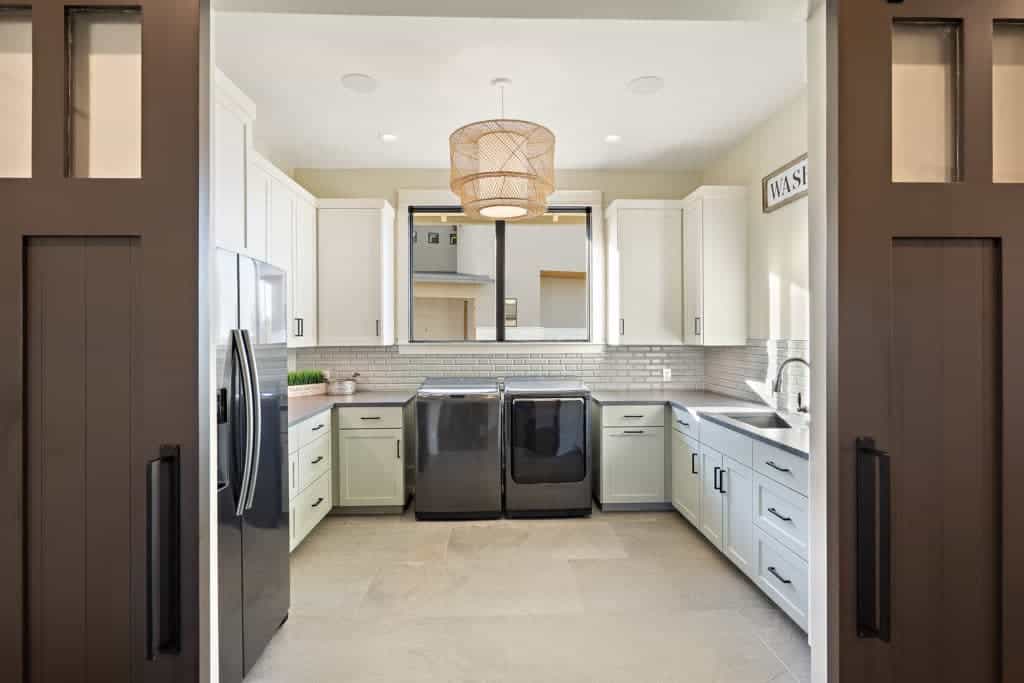 Double barn doors reveal the utility room. It is equipped with a fridge, laundry appliances, and a sink.