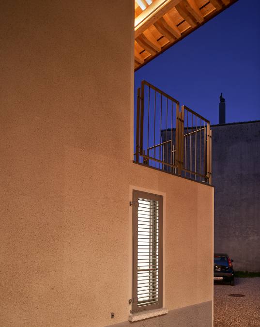 In this low-angle shot you can see the side of the building and its wall facade, as well as a dark vertical window while lights are on.