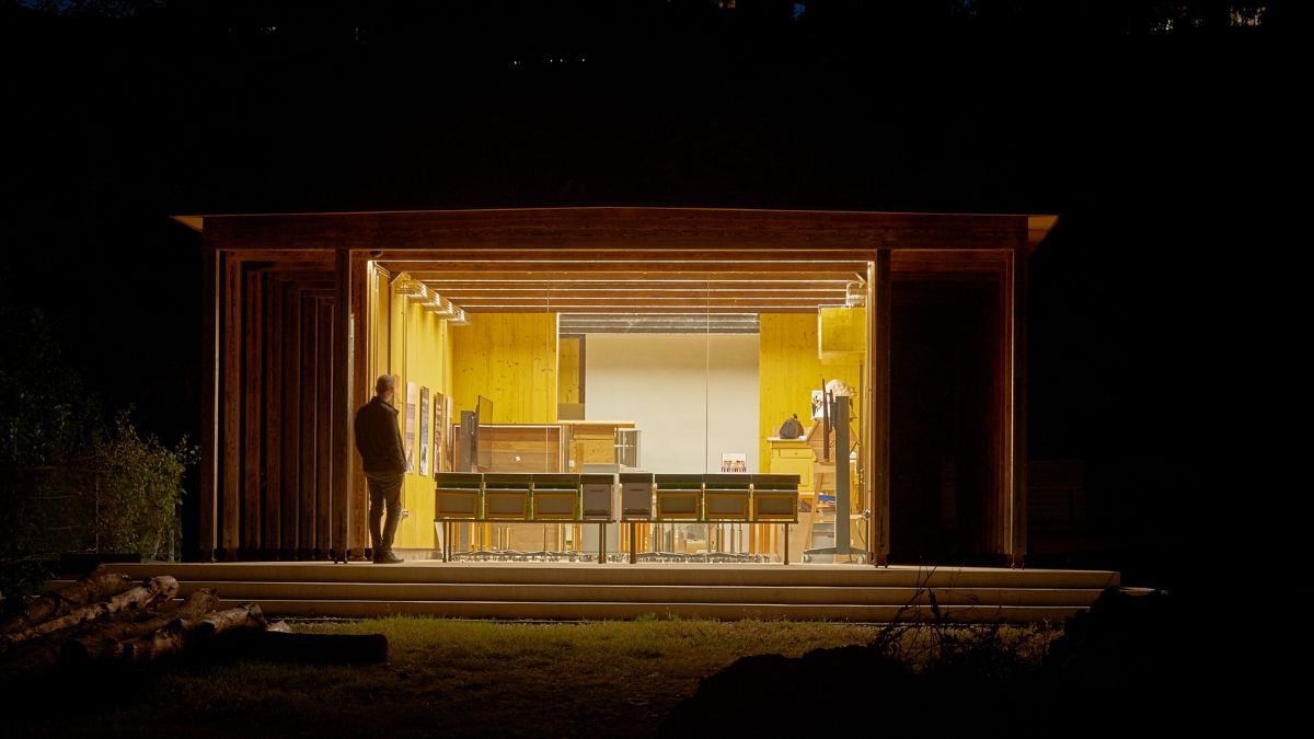 This photograph shows a night view of the pavilion with lights on, showcasing the space inside.