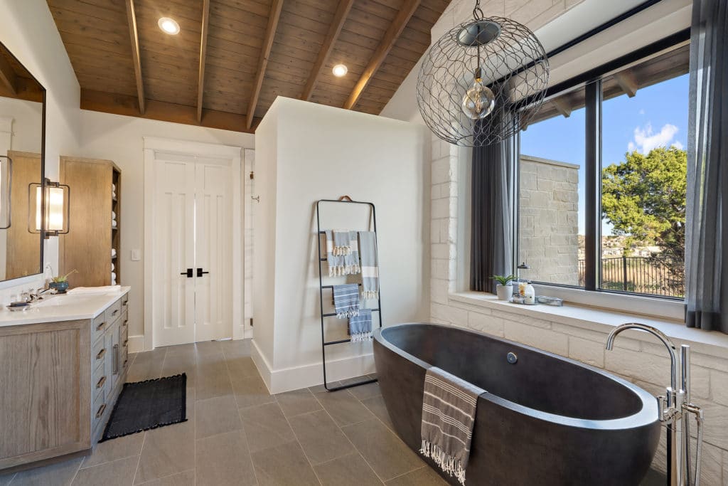 A vaulted ceiling clad in wood planks and beams tops the primary bathroom. 