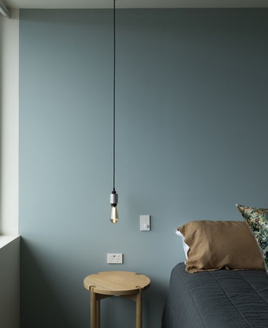 A photography of a bedroom interior design focusing on a small wooden table with a light bulb hanging on top of it.