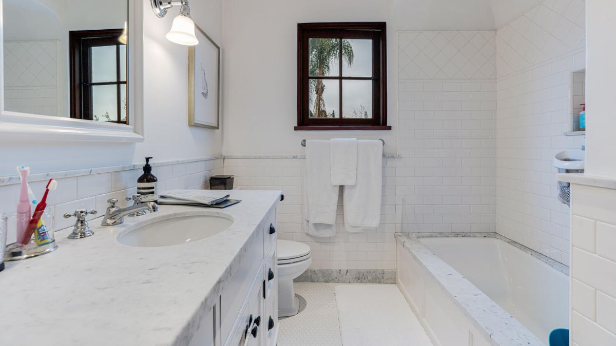 Bathroom with a completely white color scheme, including the sink, cupboards, mirror, toilet, and baththub.