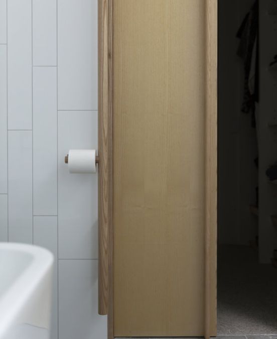 An interior shot of the bathroom focusing on the stile door and white tiled wall where tissue roll is placed.