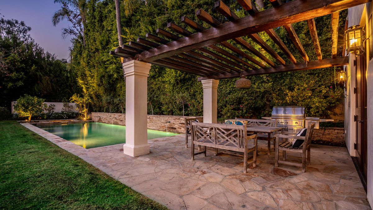 A barbecue area with an eating area that looks out over a pool shows off life at its finest.