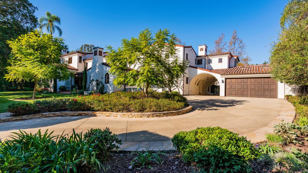 A driveway leading to the house entry is visible after passing through the gate; it is lined with attractive plants and trees.