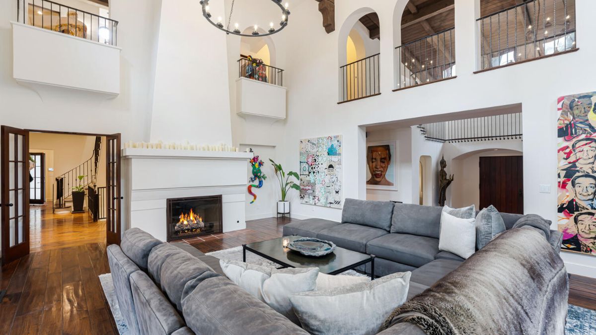 The living area has high ceilings, wood floors, an interior painted in white, and a gray sofa that complements the decor.