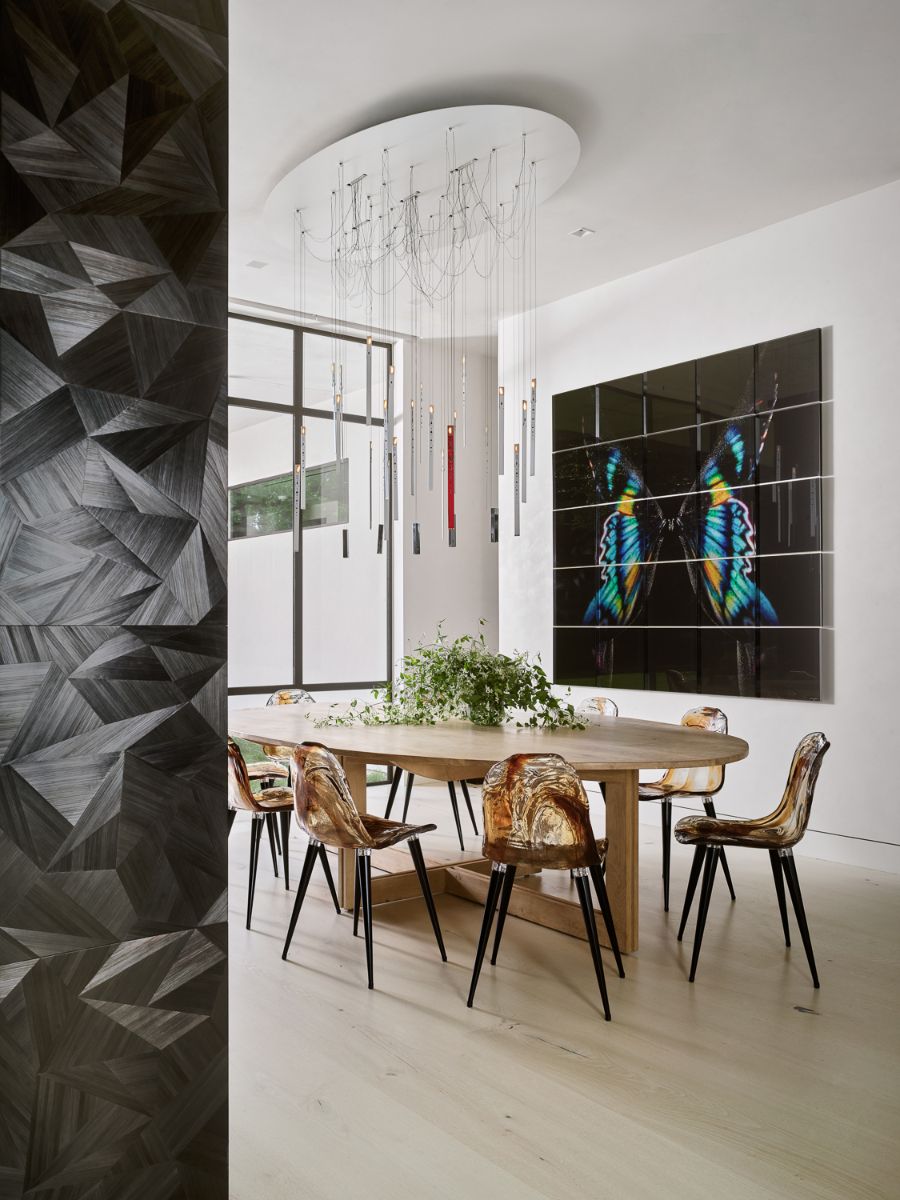 A dining area with six-seater oval dining table with artwork and custom lighting.