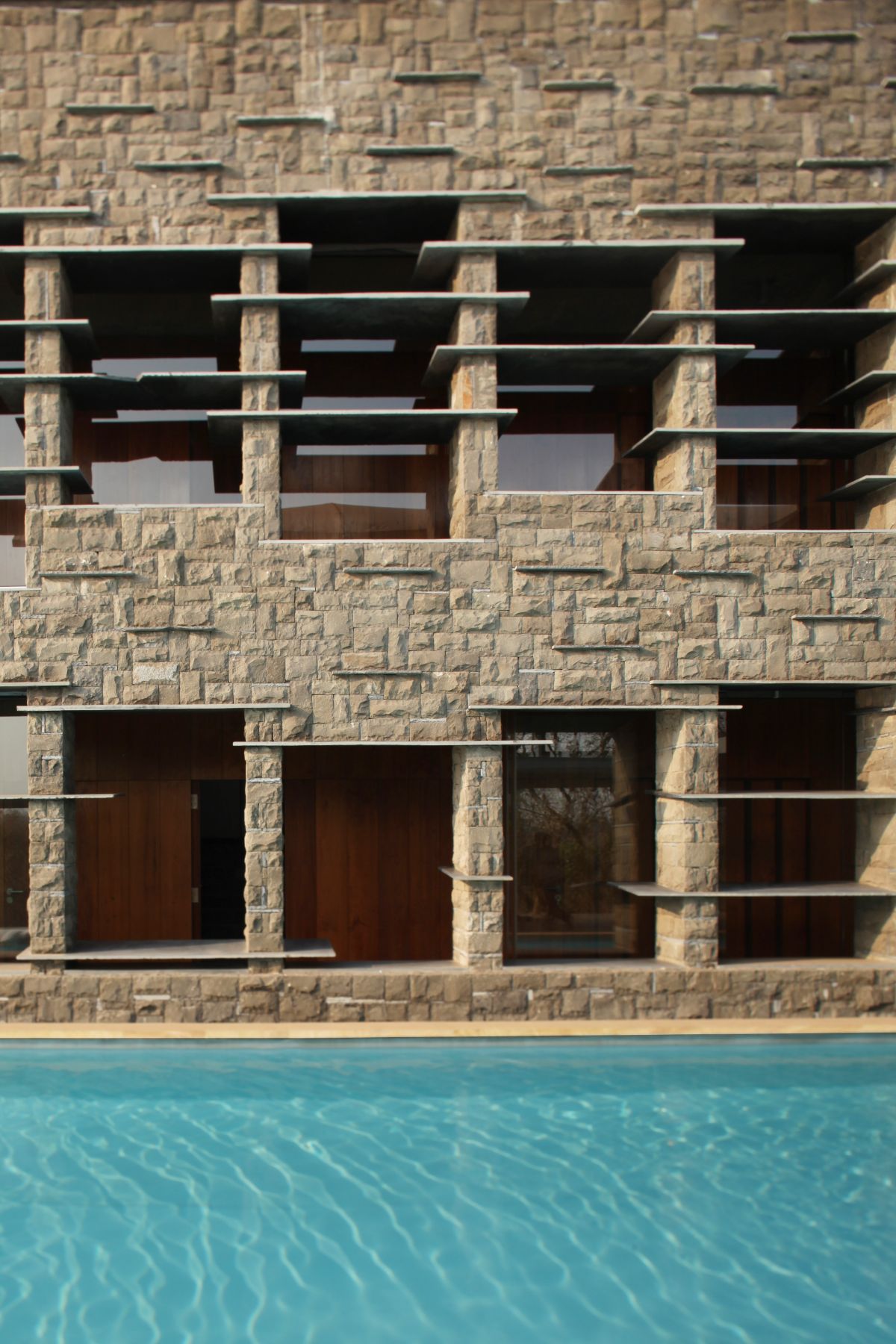 There is a pool in front and a beautiful view of the house windows with basalt stone slabs.