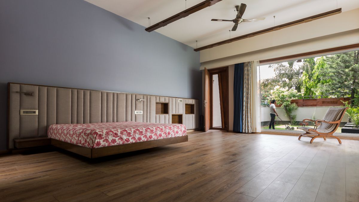 A large and light-filled bedroom with a full-width window and door leading to the lawn.