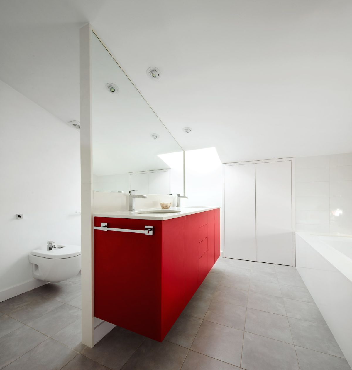 The bathroom has a floating toilet and a floating vanity. The lower part of the vanity has a red color that highlights the room.