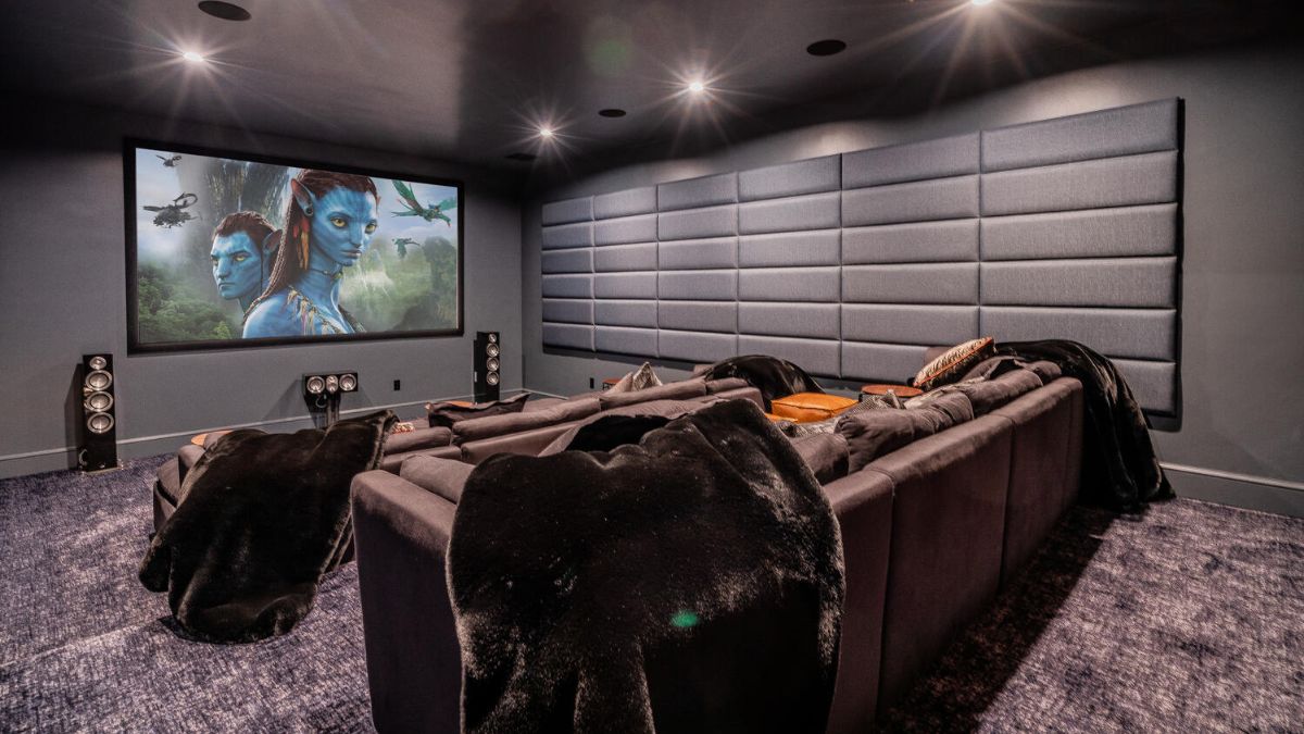 The interior of this media room on the first floor is unique from other rooms; it has a dark gray color scheme that extends from the ceiling to the wall to the sofas and carpet, and it has a large TV that everyone can view.