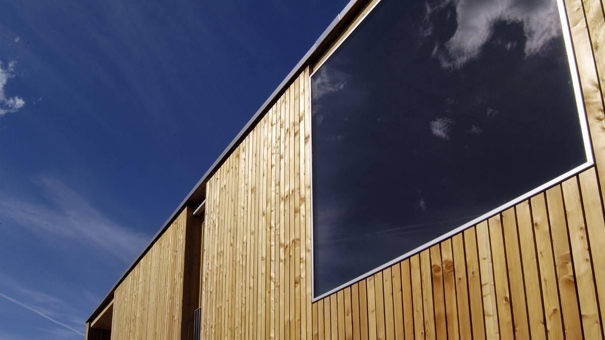 A low camera angle shows a side of Casa Duplo, which has vertical wood claddings of its wall and a glass window.