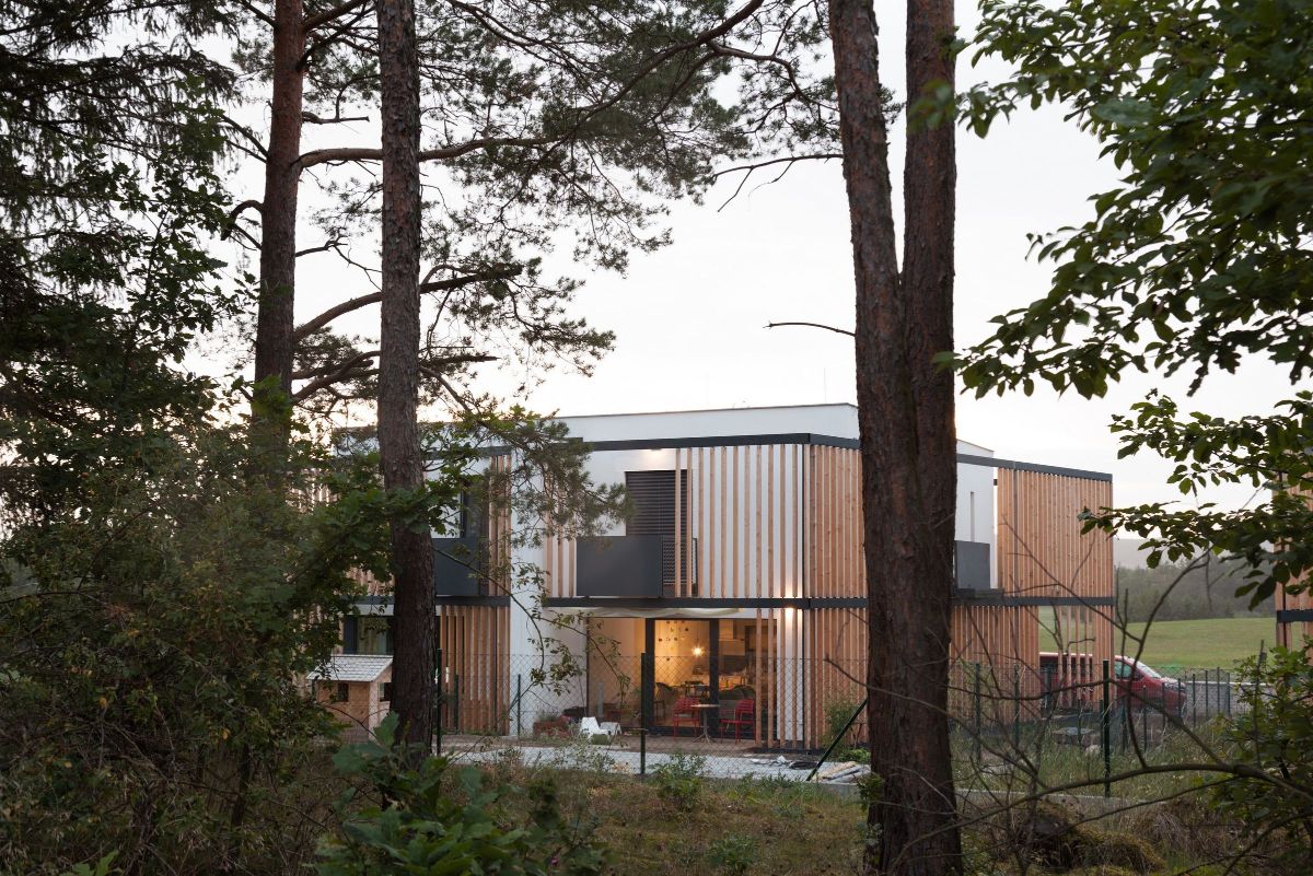 A two-story house surrounded by wooden vertical elements and hanging steel construction. 