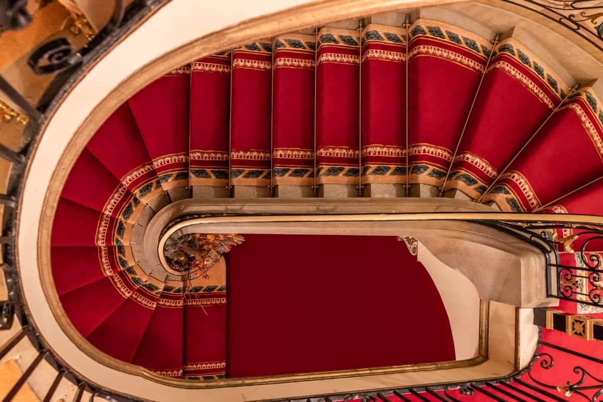 Top view of the winding staircase with marble steps dressed in an elegant red carpet.