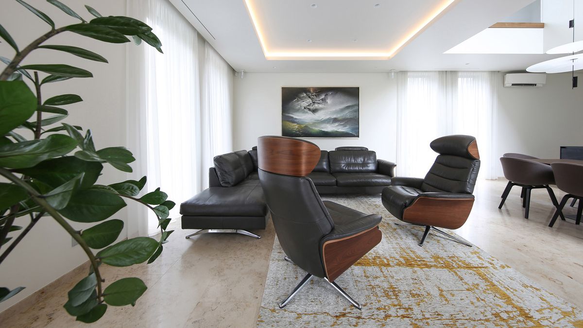 Natural Jura limestone flooring, a cozy black couch, and executive chairs with black leather complement the living room's basic white walls and curtains.