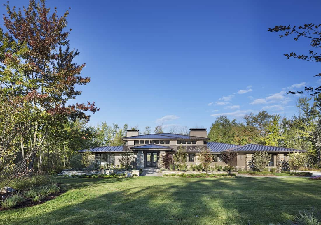 Home facade with metal hipped roofs, wood and stone siding, and a sleek entry lined by huge columns.