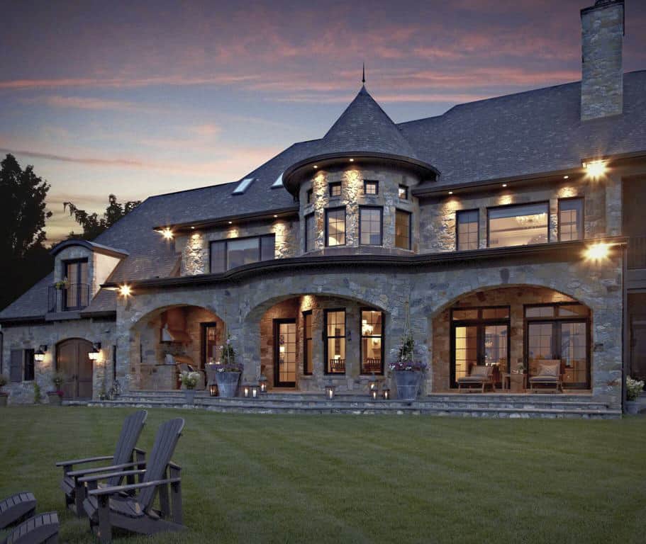 A view of the house from the backyard showcasing its charming turret and an expansive covered porch framed with stone archways.