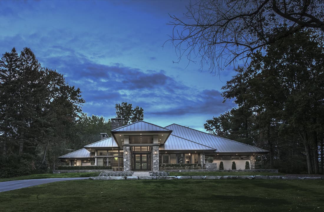 Home facade with low-pitched hipped roofs, a french front door, and a covered walkway lined with stone columns.