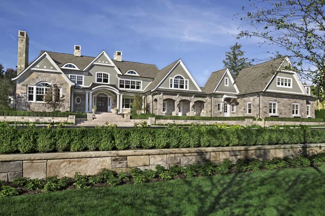 Home's sprawling facade showcasing multiple gables, a stone exterior, and decorative arches framing the windows and covered porches.