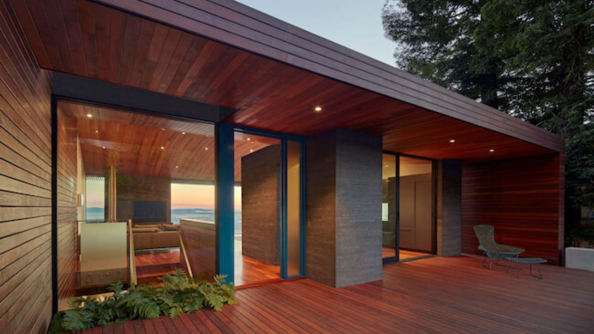 A close-up photograph highlighting the exterior design of the house, with an added perspective of the interior visible through the expansive glass walls.