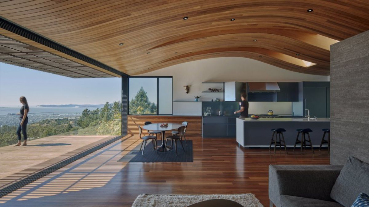 The photograph depicts an interconnected interior space that encompasses the living, dining, and kitchen areas, extending seamlessly to an outdoor deck. Additionally, the image captures an impressive view of Oakland city that can be seen from this vantage point.