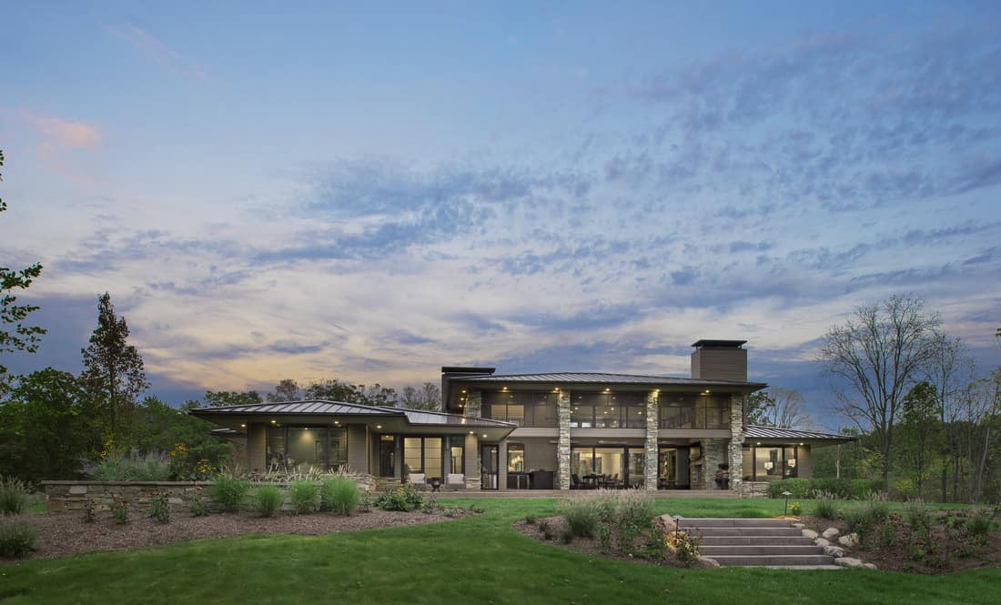 View of the house from the backyard featuring its sprawling outdoor space and expansive glazing.