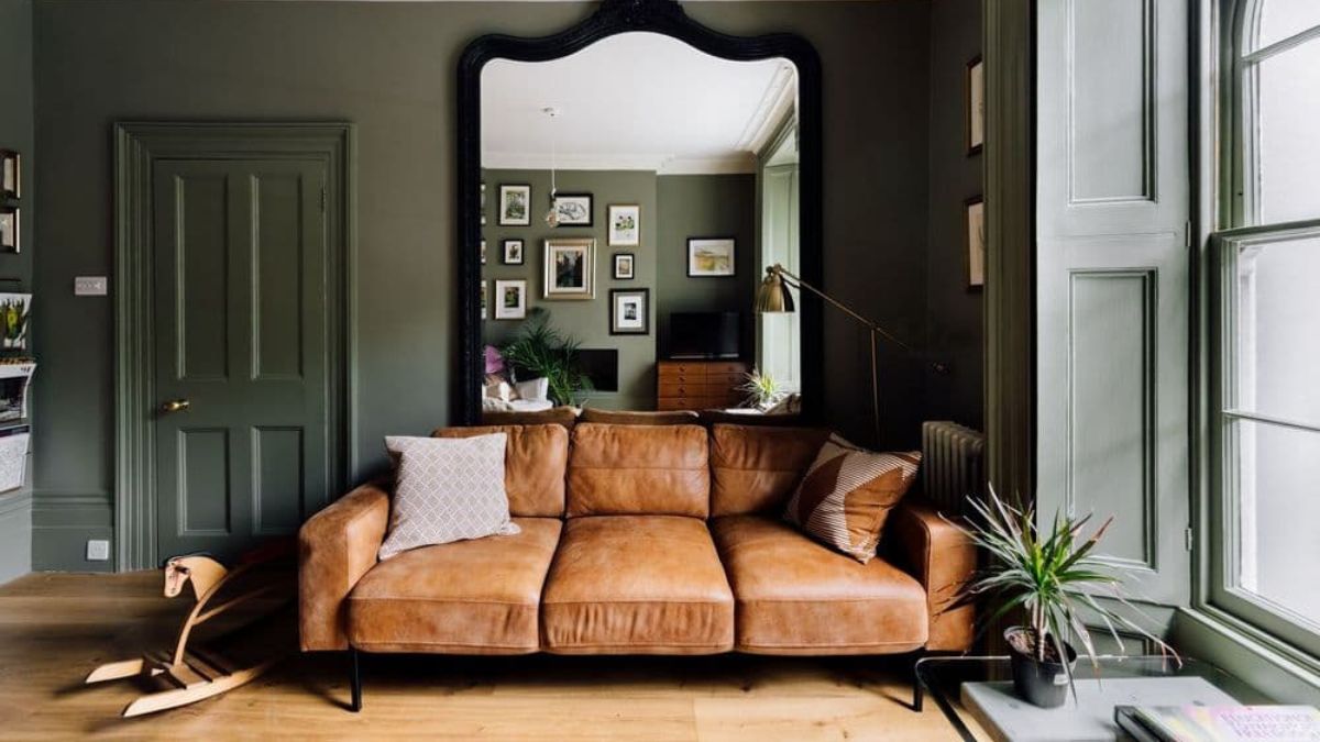 The three-seater light-brown sofa in the living room contrasts with the dark-colored atmosphere of the room.