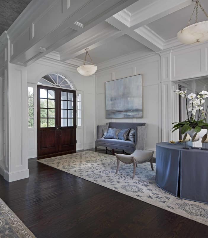 A french front door welcomes guests into the foyer. It has a velvet bench and a matching skirted round table.