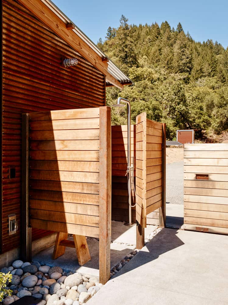 The outdoor shower is encased in wood planks and has a concrete floor bordered by pebbles.