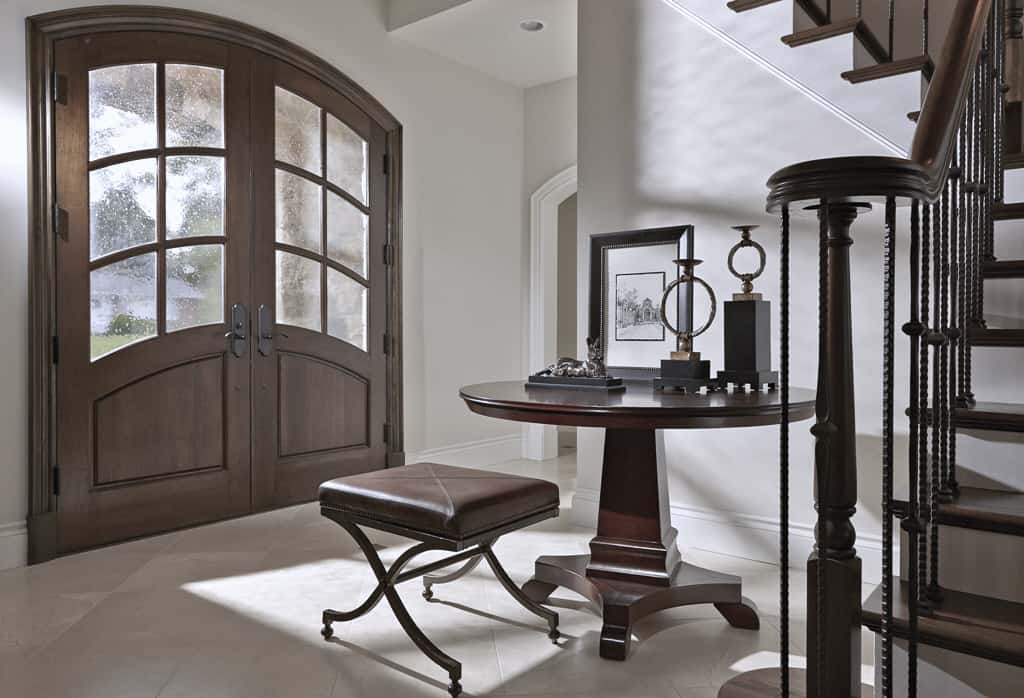 A french front door opens into the foyer. It is furnished with a round center table and a leather cushioned stool.