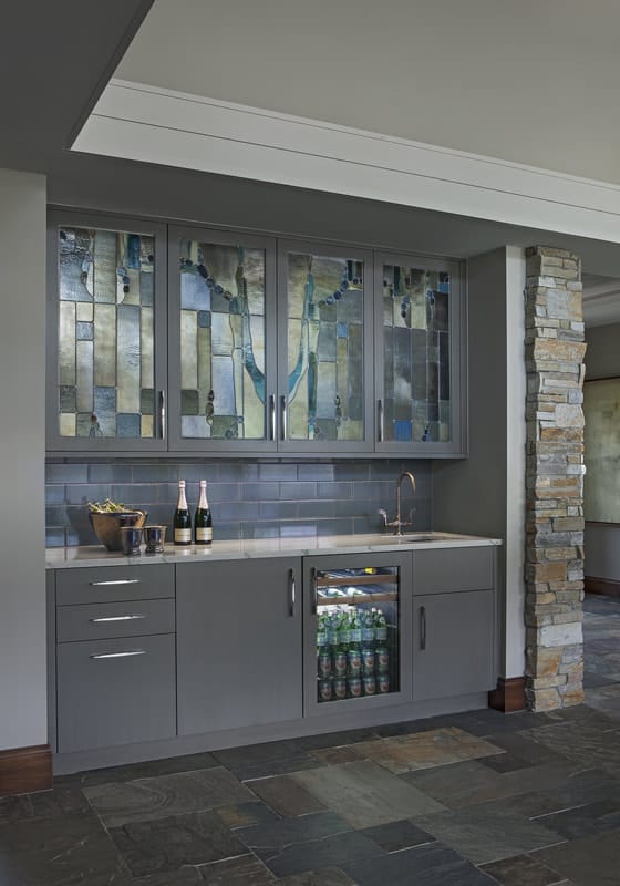 A wet bar across is adorned with custom cabinets and subway tile backsplash.