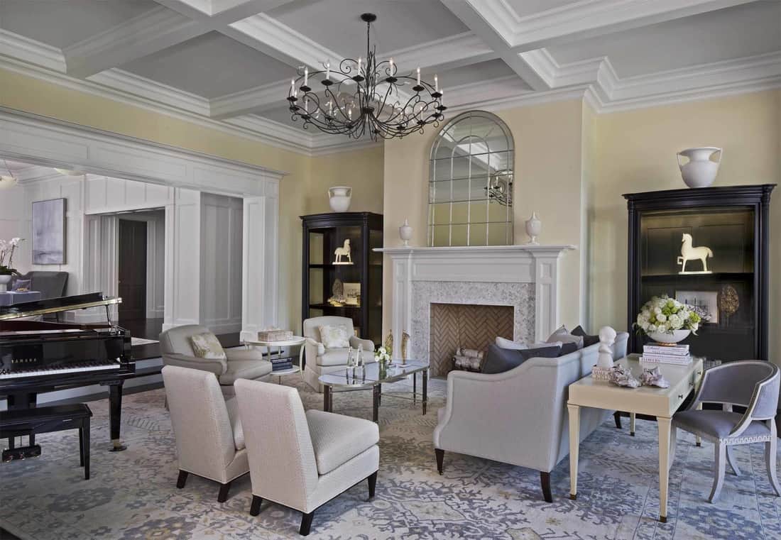 The living room is filled with gray seats, a fireplace, a desk, and a baby grand piano.