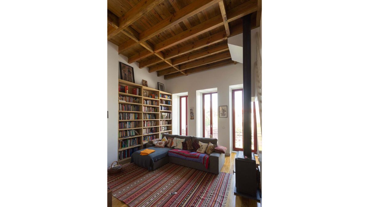 The living area contains book shelves, concrete white walls, a carpeted floor, and hardwood ceiling and flooring.