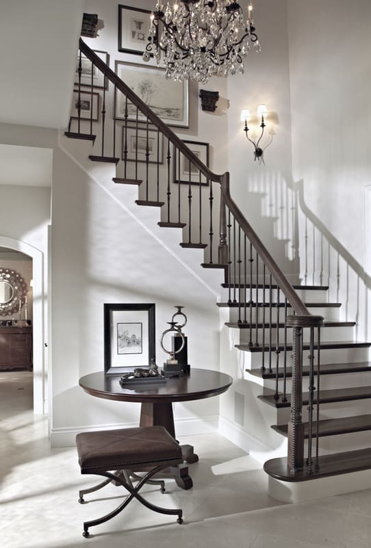 The foyer includes a winding staircase illuminated with wrought iron sconces and an elegant crystal chandelier.