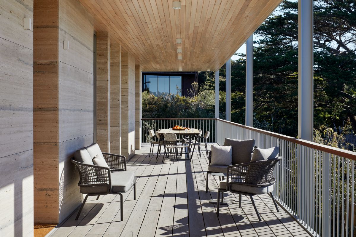 The balcony features an outdoor dining table and offers a view of the surrounding trees.