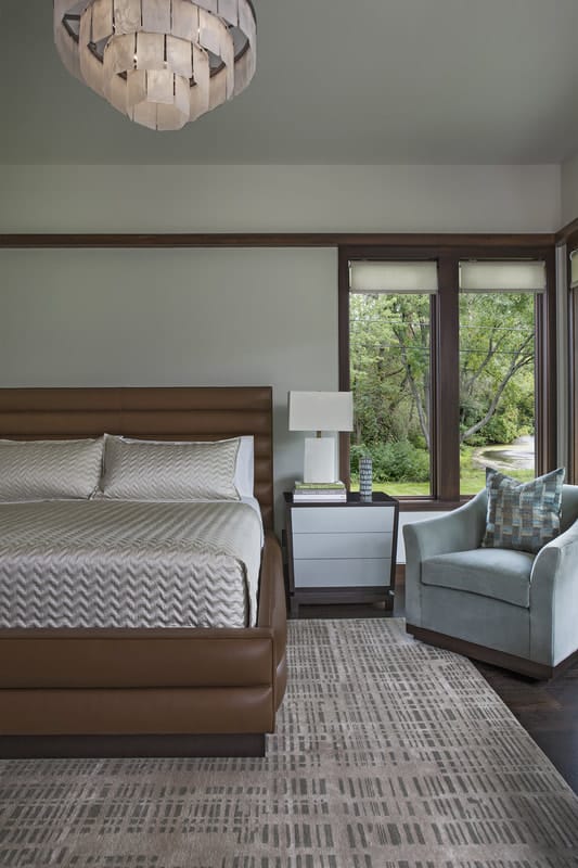 A contrast of brown leather bed and light armchair adds interest to the primary bedroom.