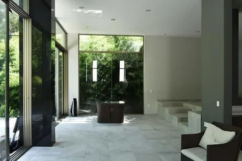 This is an interior photograph of a spacious living room with marble flooring and massive glass wall panels.