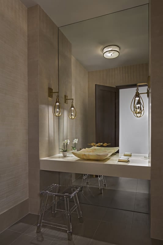 A marble vessel sink complemented with a glass stool brings elegance to the powder room.