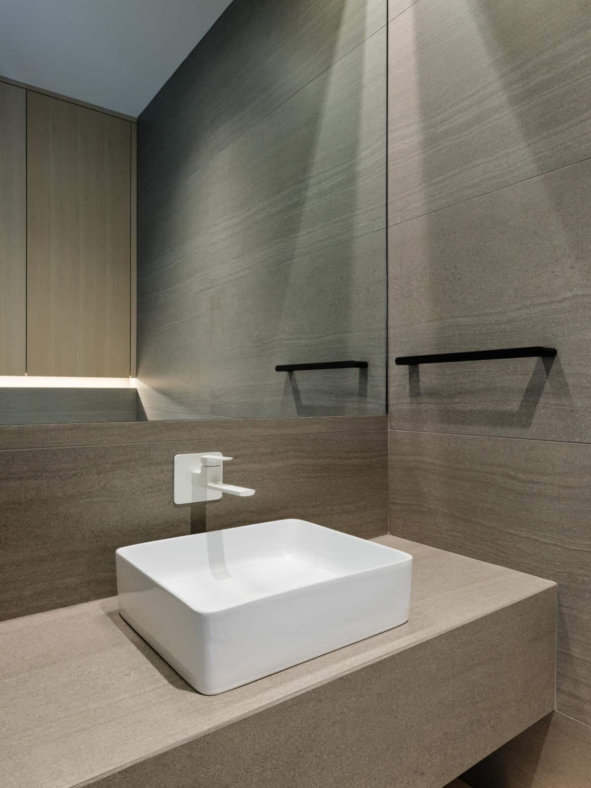 The modern aesthetic continues to the bathroom with a frameless mirror and a sleek vessel sink.