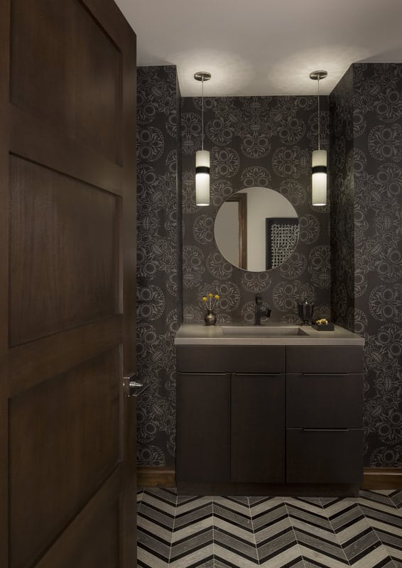 This powder room is adorned with patterned wallpaper and a chevron-tiled floor.