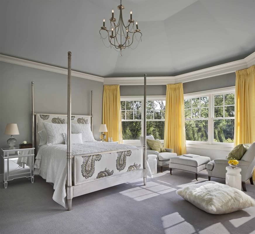 This bedroom mimics the primary suite's layout. It offers gray seats and a four-poster bed complemented with mirrored nightstands.