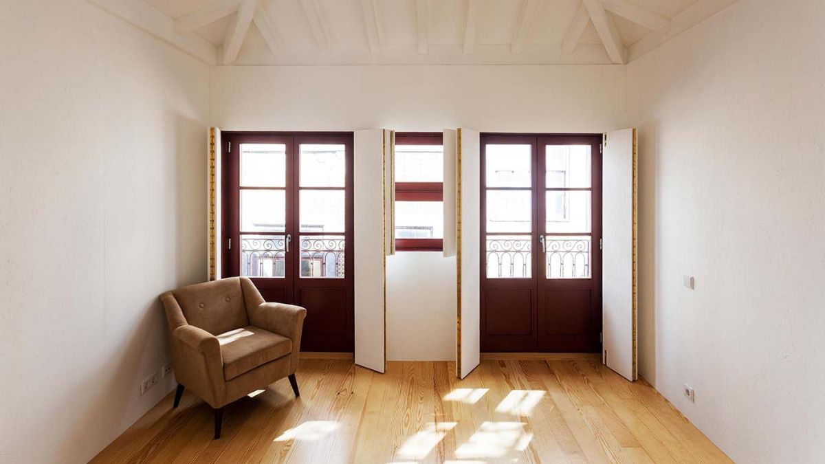 This open area, which is a portion of the living room, has two wooden-glass doors, white walls, and wood floors.