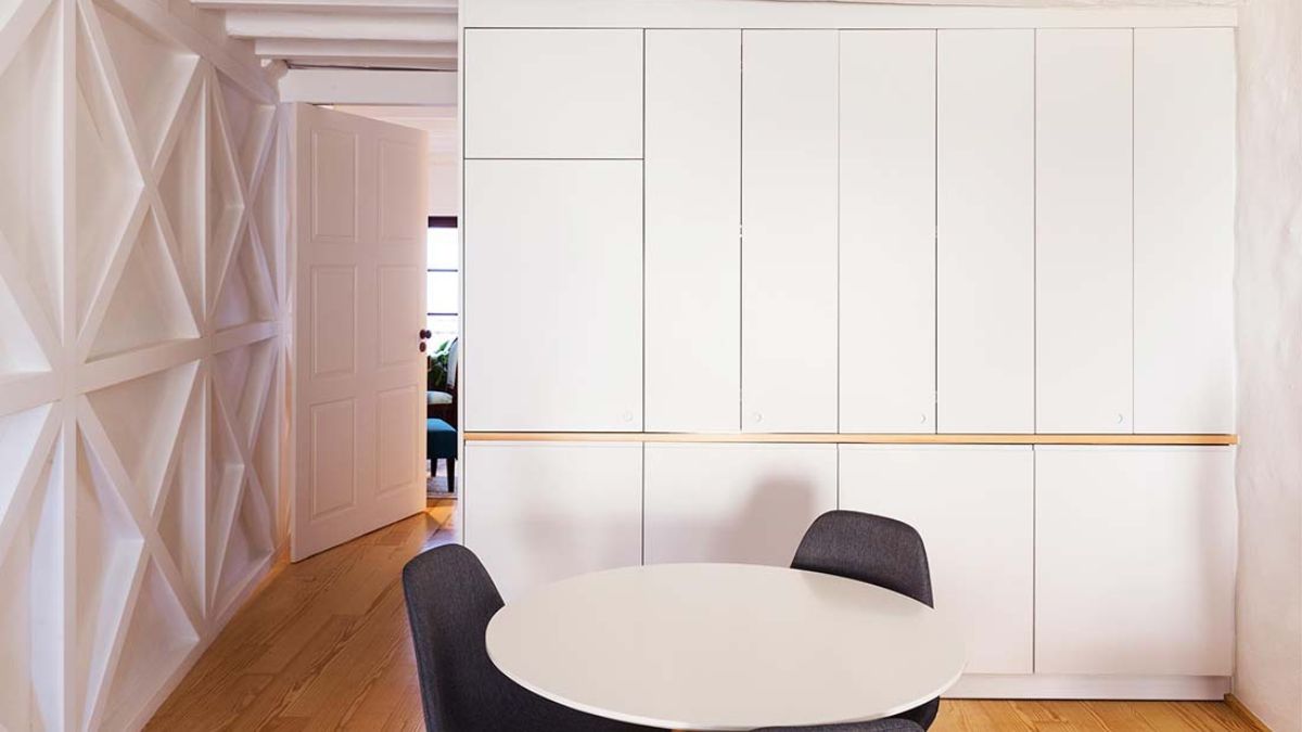 In the dining room of this home, there is a little circular white table with gray stylish seats and white cabinetry.