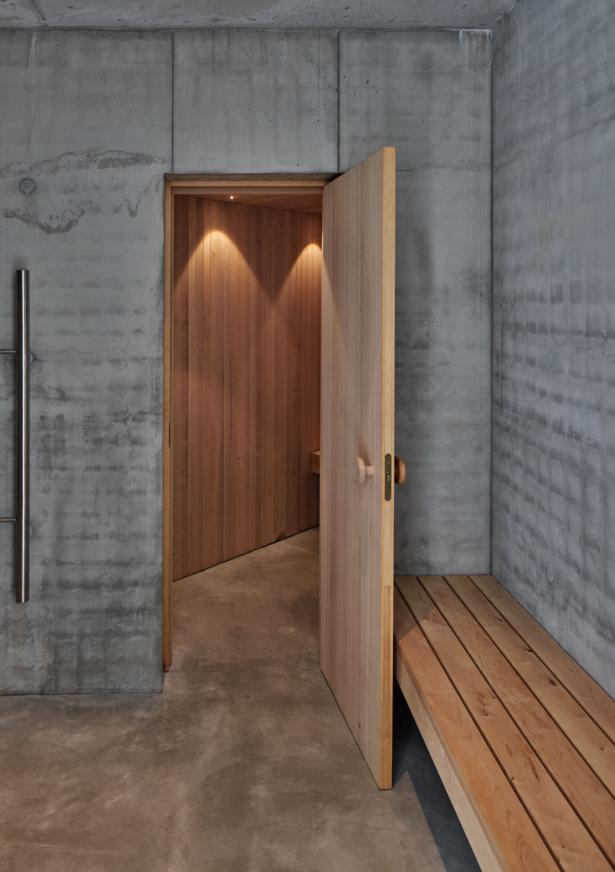 The bathroom features a wooden bench that blends well with the exposed concrete left on purpose.